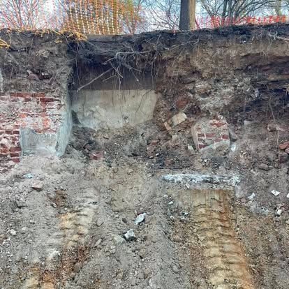 Excavated dirt wall with exposed brick and concrete, showing a rough cut into the earth and tracks below