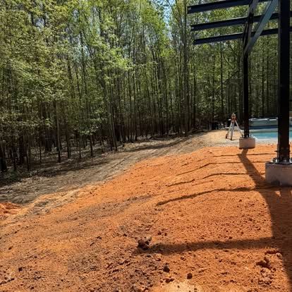 Dirt path beside a bamboo grove, with a pool and pergola casting shadows in bright sunlight.