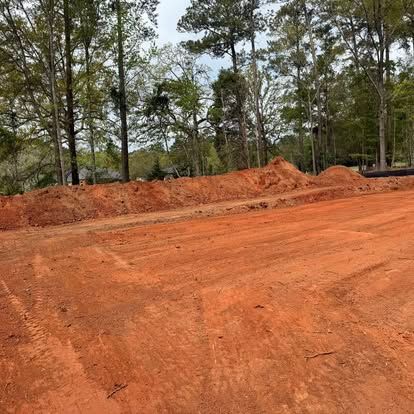 Red dirt construction site with graded soil and tall trees in the background
