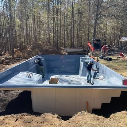 Workers installing a white in-ground pool shell in a wooded backyard