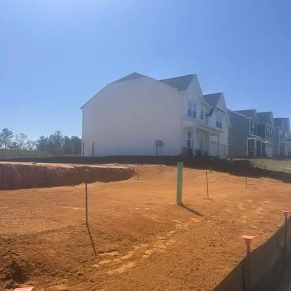 New houses under construction on a red dirt lot beside a road on a sunny day