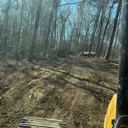 View from a yellow construction vehicle on a muddy dirt road through a leafless forest
