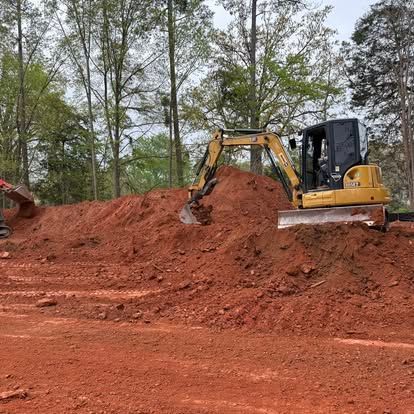 Yellow excavator digging red dirt on a mound at a wooded construction site