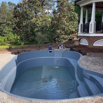 Empty backyard swimming pool under construction beside a white gazebo and trees