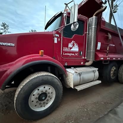 Red Kenworth dump truck parked on a dirt lot, side view.
