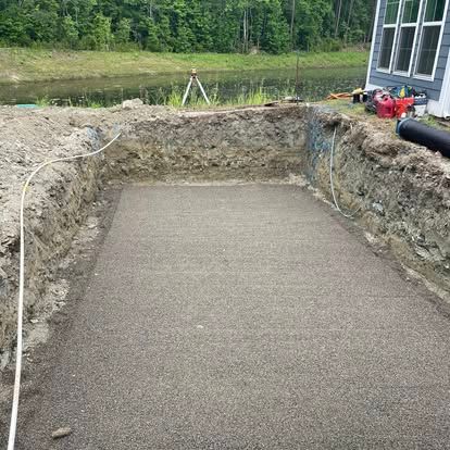Excavated backyard with a gravel base beside a house, ready for construction or landscaping