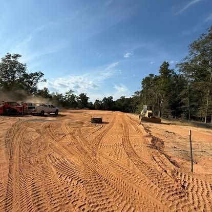 Cleared dirt construction site with heavy equipment, parked trucks, and tire tracks under a blue sky
