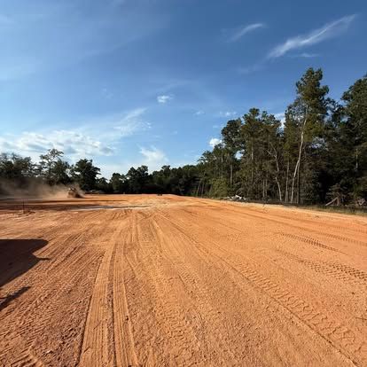 Wide red dirt road curving through a pine forest under a blue sky
