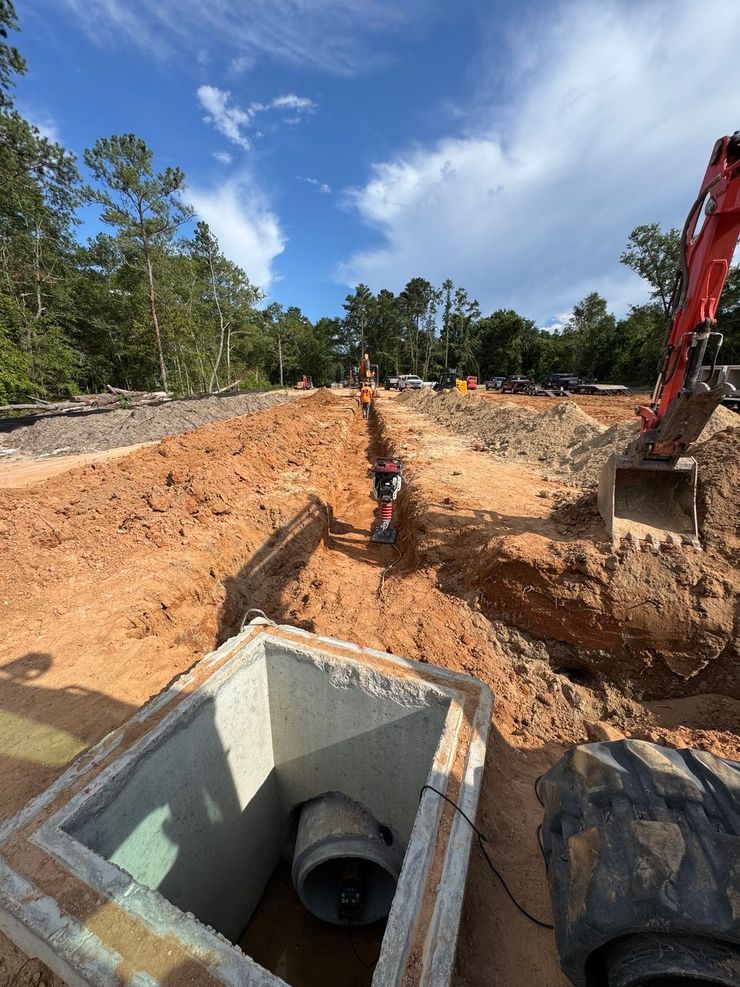 Excavation site with trench, concrete utility box, workers, and red excavator under a blue sky