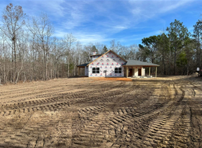 House under construction on a cleared lot with a dirt yard and trees in the background