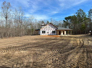 Cleared dirt lot with a white house under construction beside a wooded treeline and blue sky
