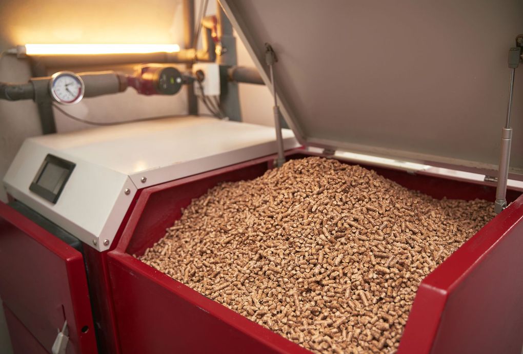 Contenitore rosso per cereali, riempito di avena o semi, illuminato da una luce industriale.