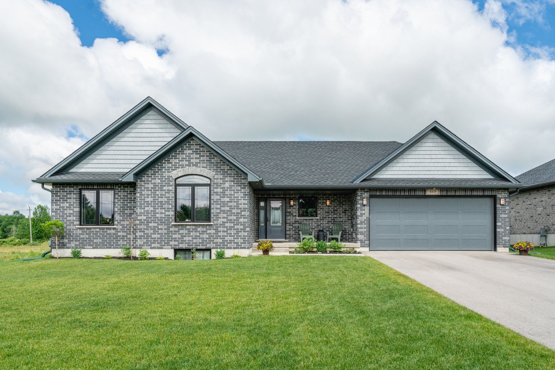 A large brick house with a gray garage door and a large lawn in front of it.