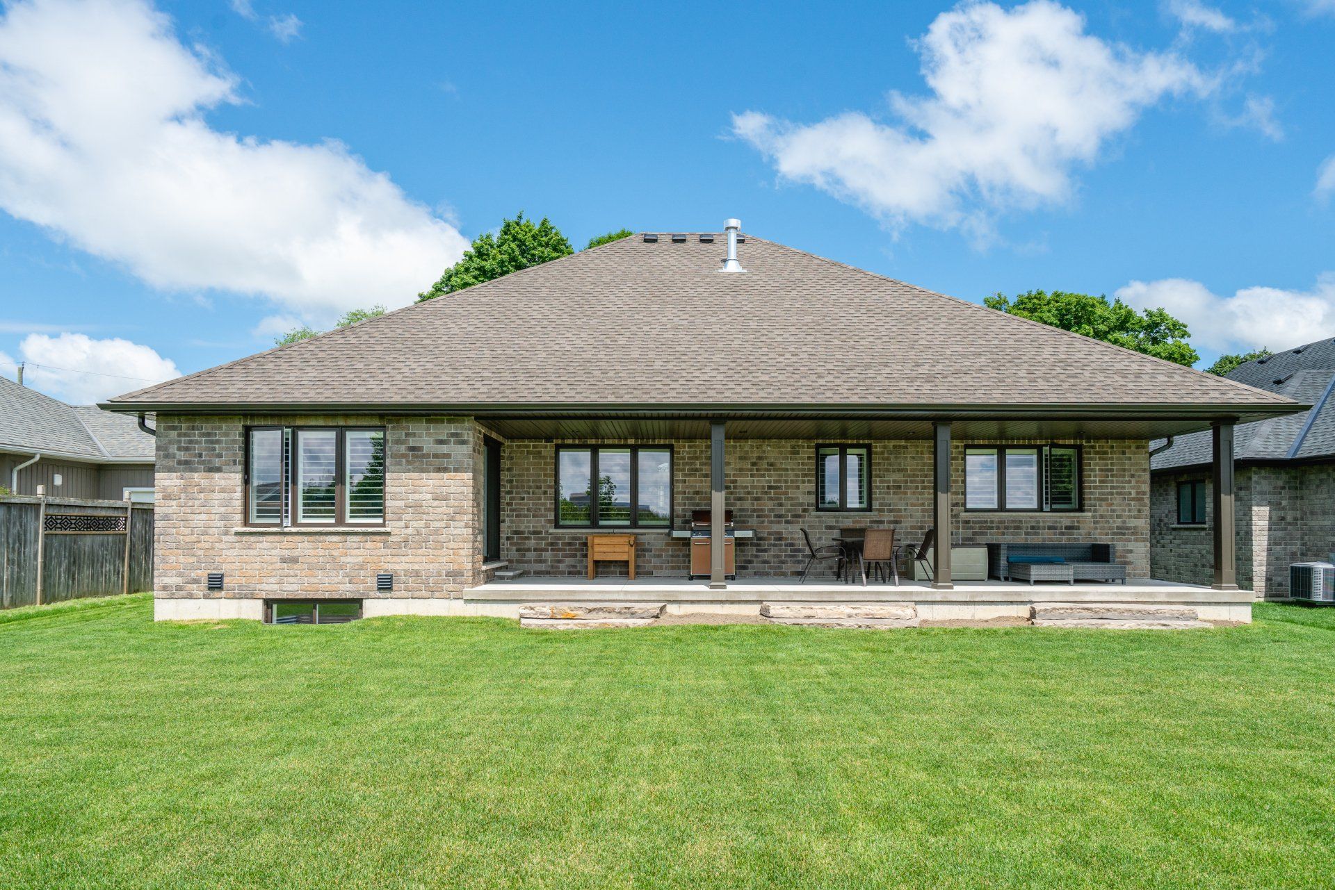 The back of a brick house with a large lawn in front of it.