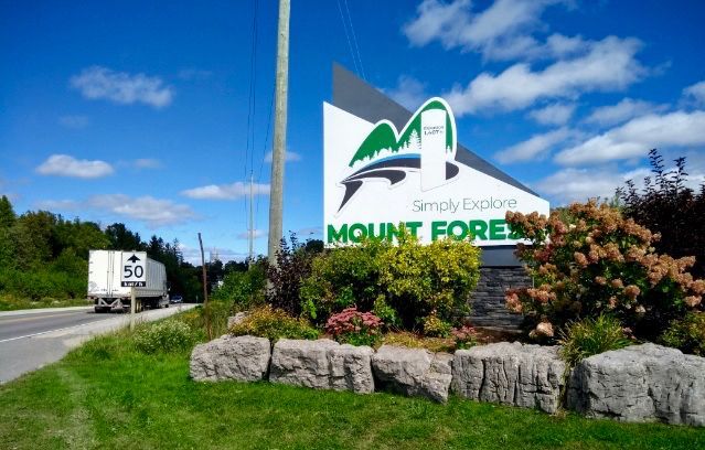 A white truck is driving down a road next to a sign that says mount forest.