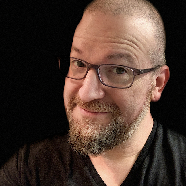 Smiling person with glasses and a beard against a black background