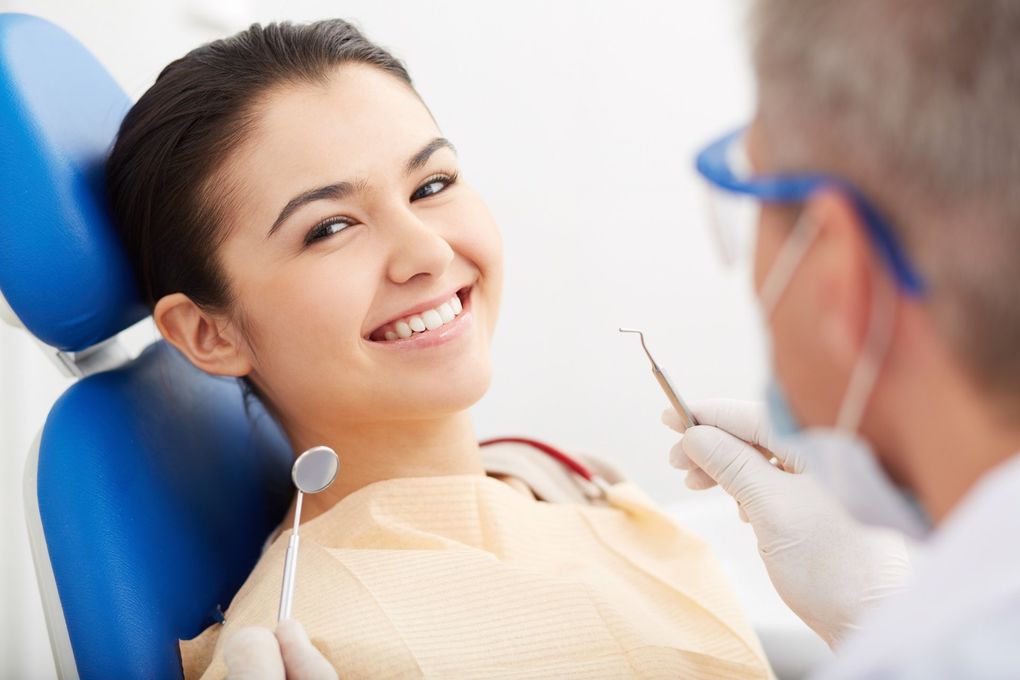 Paziente sorridente sulla poltrona del dentista mentre quest'ultimo la esamina con uno strumento.