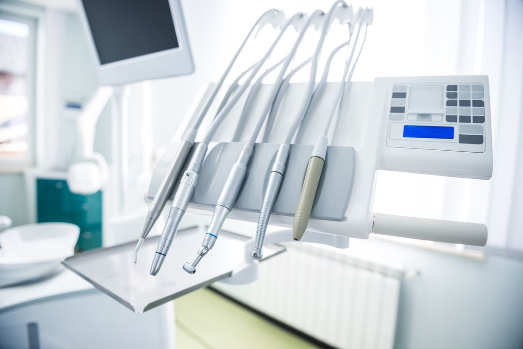 Strumenti odontoiatrici su un vassoio accanto a una poltrona da dentista in una clinica luminosa.