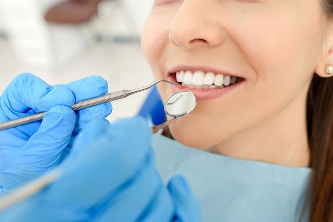 Pulizia dentale effettuata con mani guantate e strumenti appositi sui denti di un paziente sorridente.
