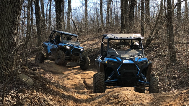 Two atvs are driving down a dirt road in the woods.