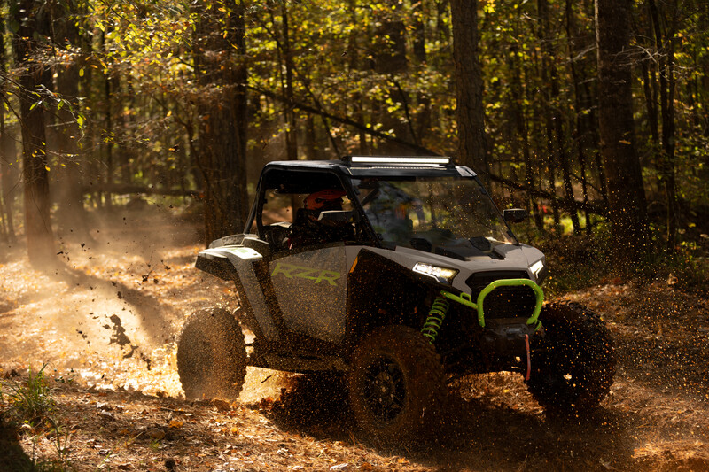A white atv is driving down a dirt road in the woods.