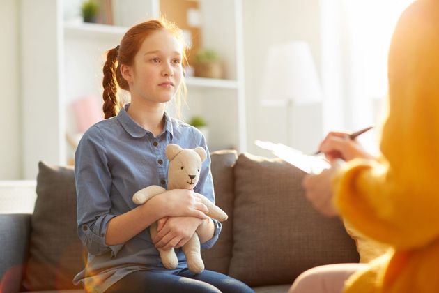 Woman holding a teddy bear during a conversation on a couch in a bright living room