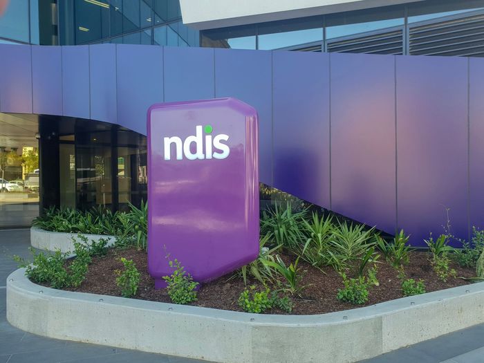 Purple NDIS sign in front of a modern building and landscaped planter bed