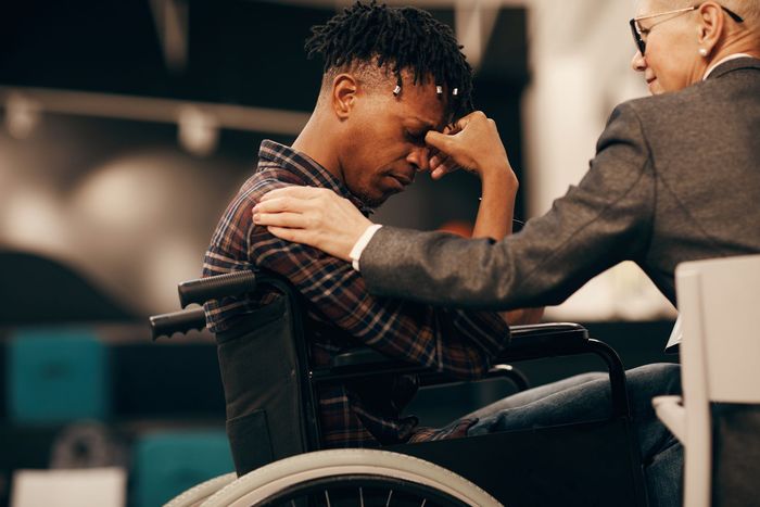 Man in wheelchair is comforted by another person in a meeting room