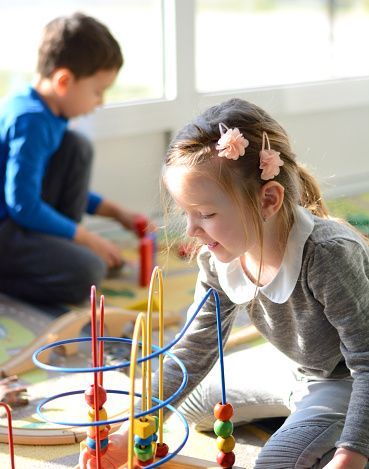 Children playing with colorful bead maze toys in a bright classroom setting