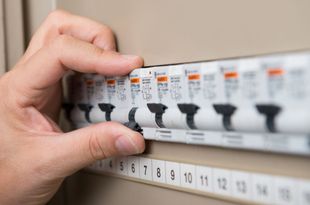 Hand flipping a circuit breaker switch in a gray electrical panel.