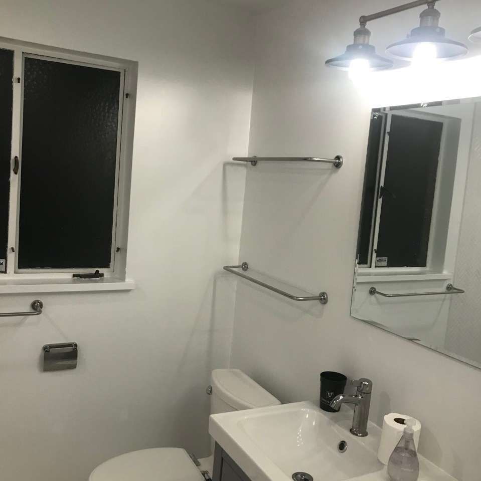 White bathroom with toilet, sink, mirror, window, and towel racks.