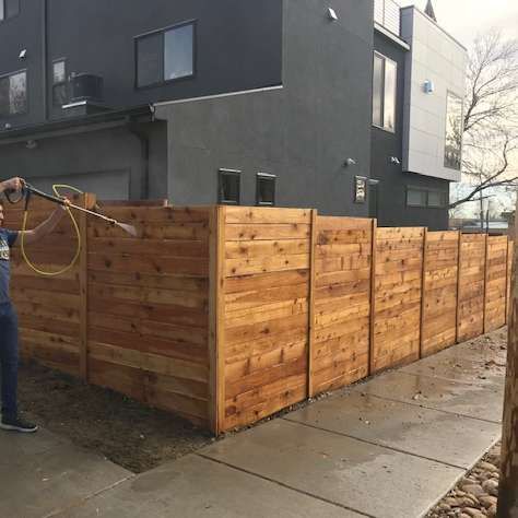 Wooden privacy fence around a sidewalk corner beside a dark apartment building.