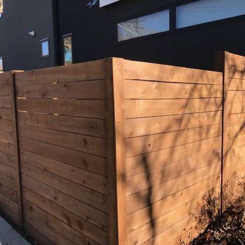 Wooden fence in front of a dark building, with horizontal planks and a corner.