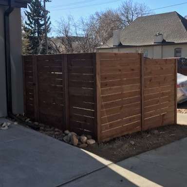 Wooden privacy fence enclosing a side yard beside a concrete driveway, with houses and trees in the background.