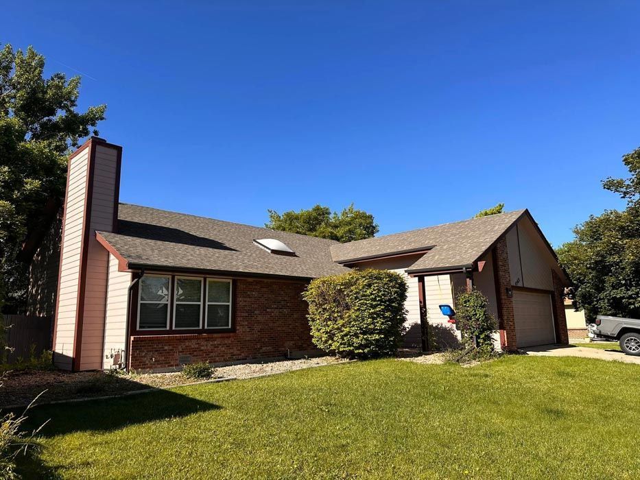 Residential house with red brick and pink siding under a blue sky, with a chimney and garage.