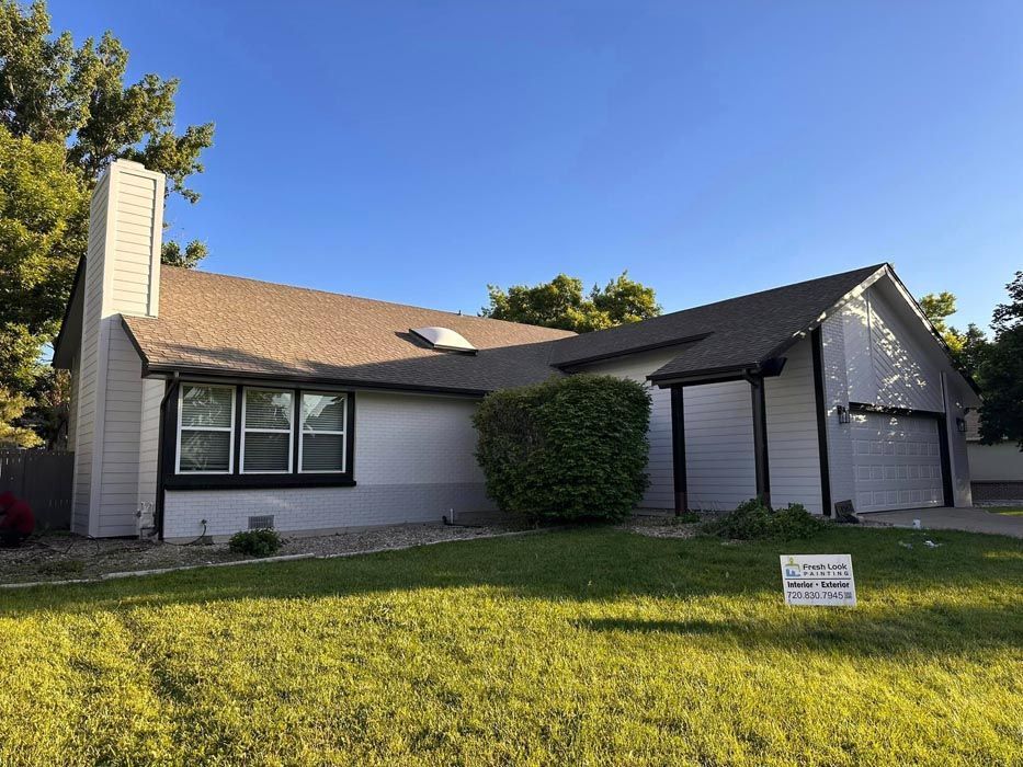 House exterior with gray siding, brown roof, and green lawn under a blue sky.