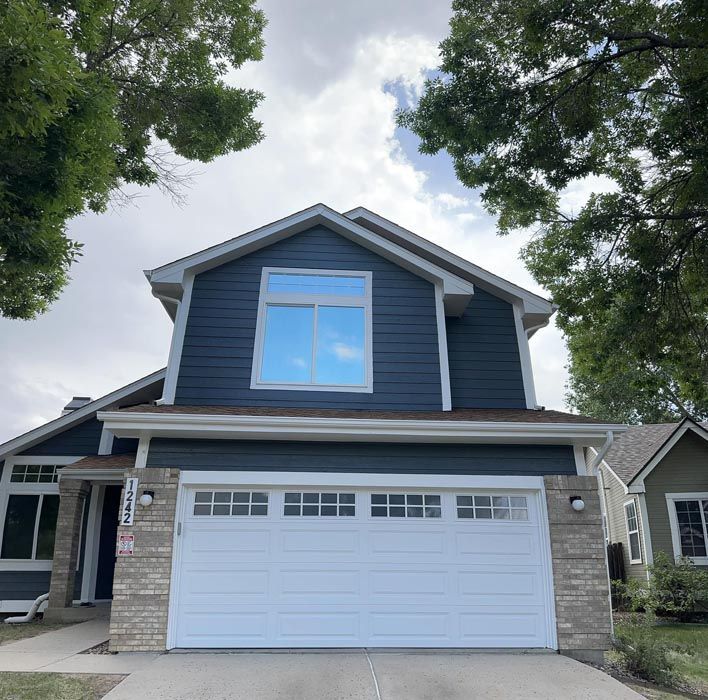 Two-story house with dark blue siding, white garage door, and light stone accents, under a cloudy sky.