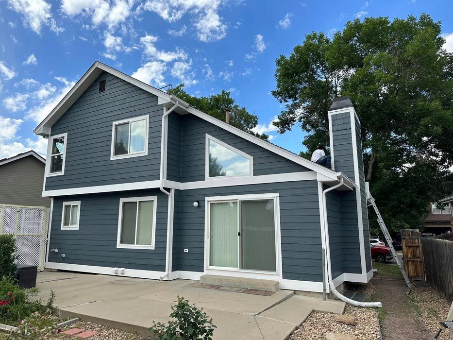 Two-story house with dark blue siding, white trim, and a concrete patio on a sunny day.