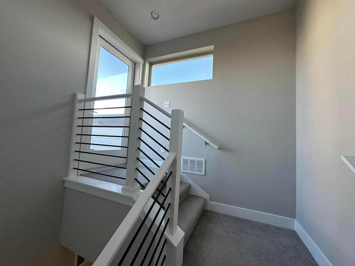 Empty staircase landing with gray walls, white railings, and windows letting in daylight