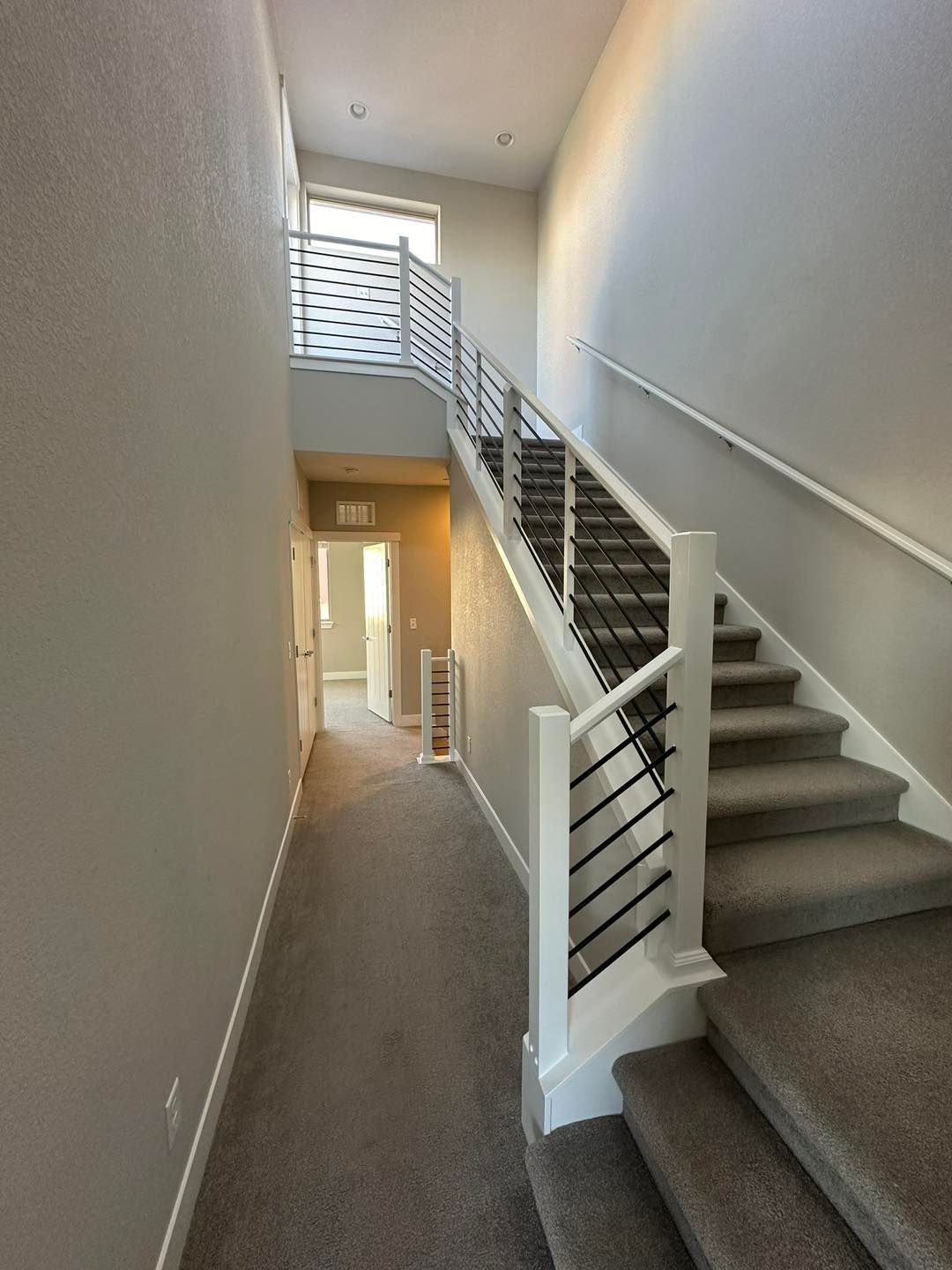 Interior stairwell with gray carpeted stairs, white walls, and a windowed landing.