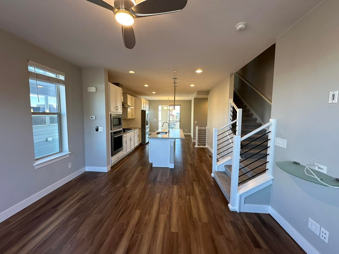 Open-concept living room and kitchen with dark wood floors, staircase, and large windows