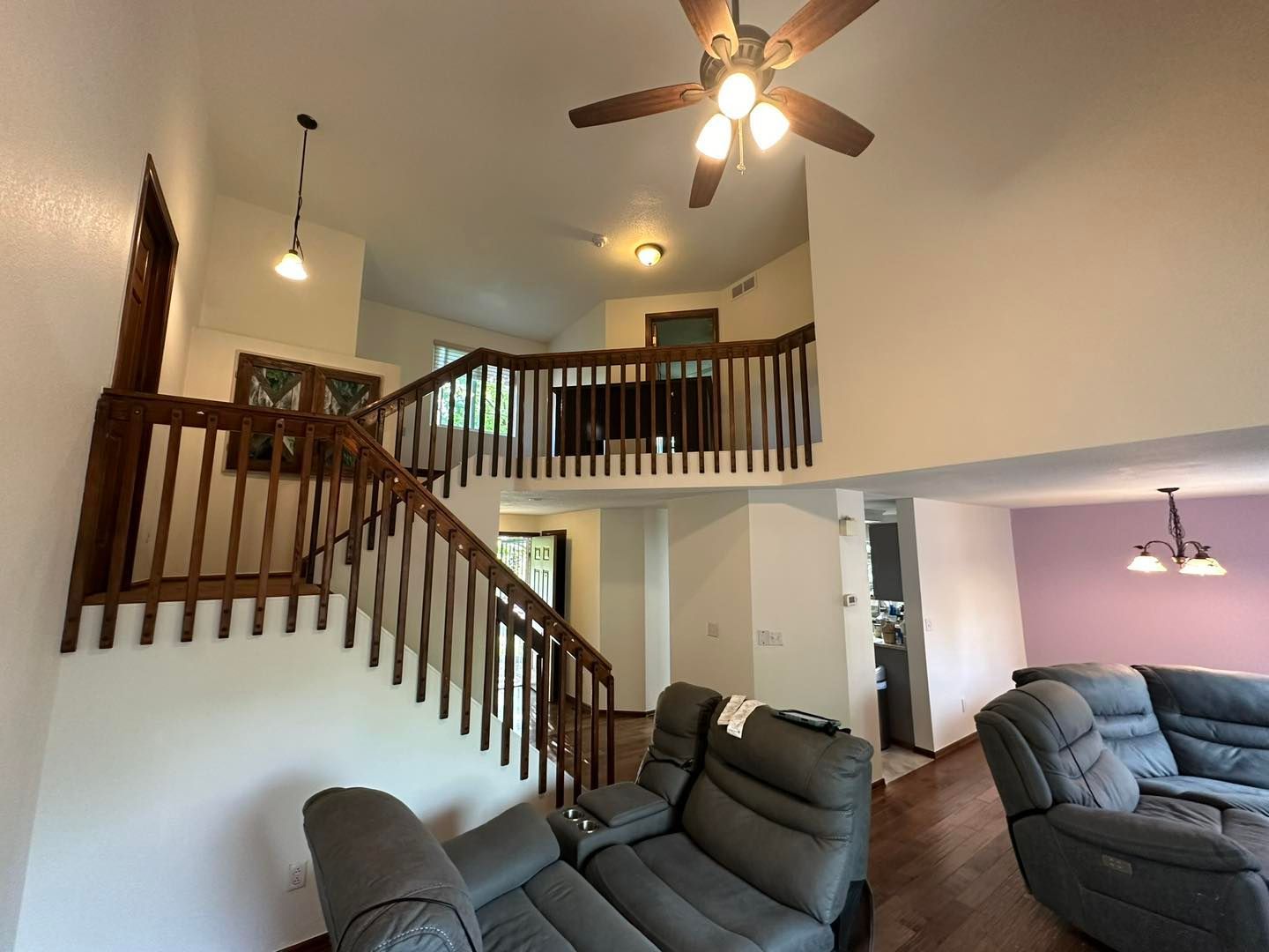 Living room with staircase, vaulted ceiling, ceiling fans, and gray recliners