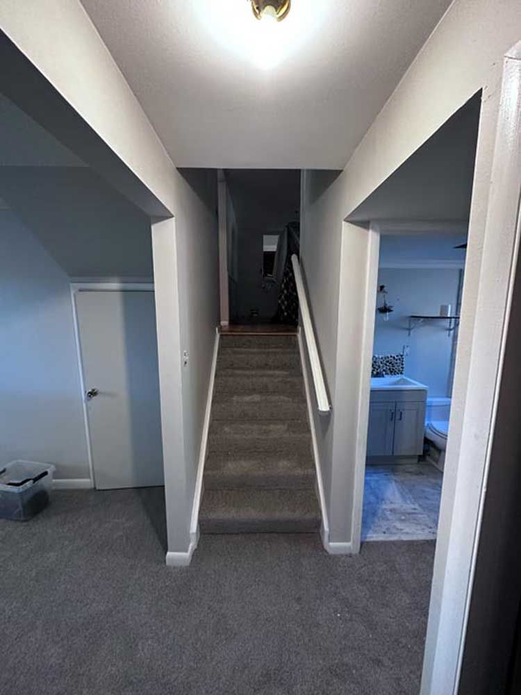 Hallway with carpeted stairs leading up between two open doorways, one showing a kitchen.