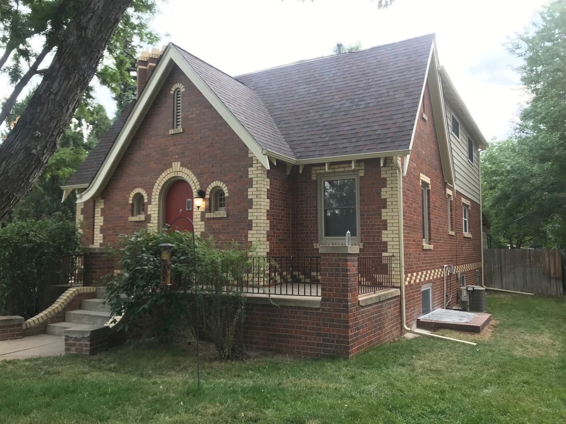 Red brick house with a dark brown roof and light-colored trim, surrounded by grass and trees.