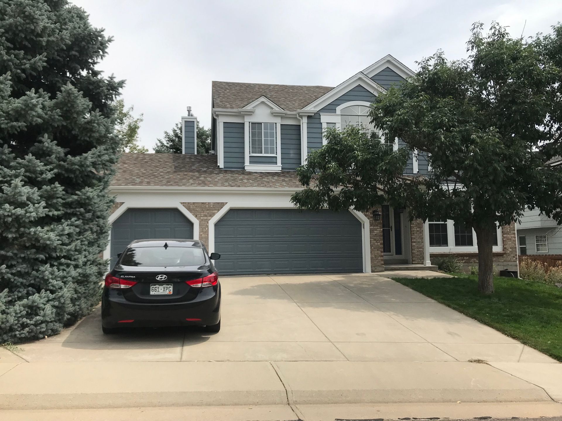 Two-story house with blue siding, two-car garage, and a black car parked in the driveway.
