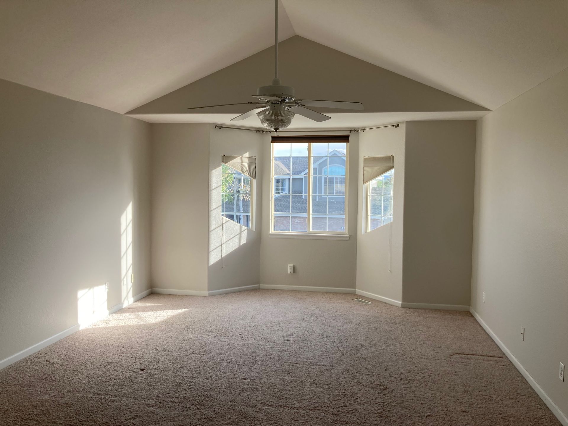 Empty room with slanted ceiling, large window, carpet, and a ceiling fan.