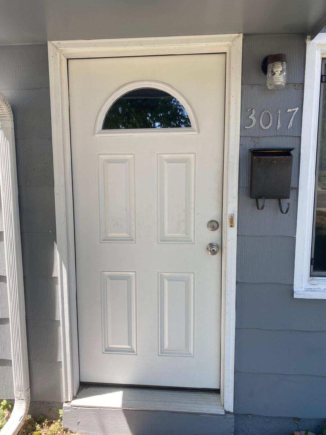 White front door with arched glass, mail slot, house numbers, and gray siding.