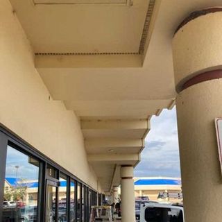 A store exterior with a beige overhang, support columns, and storefront windows with a cloudy sky in the background.