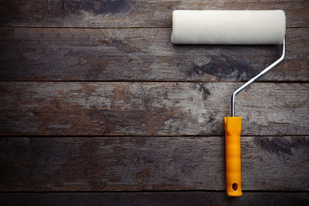 Paint roller with white roller on weathered, brown wooden planks.