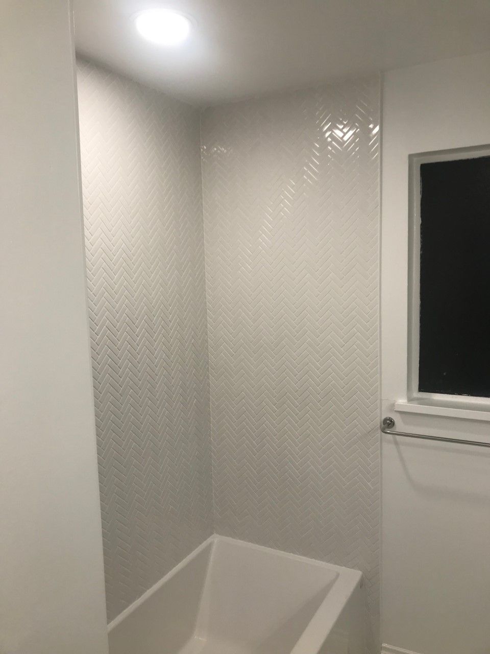 White-tiled bathroom corner with a built-in tub, a window, and a towel rack.
